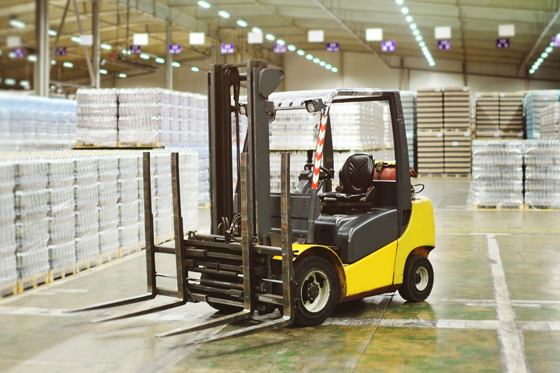 Carretilla elevadora amarilla en alamacén rodeada de palets de mercancía.